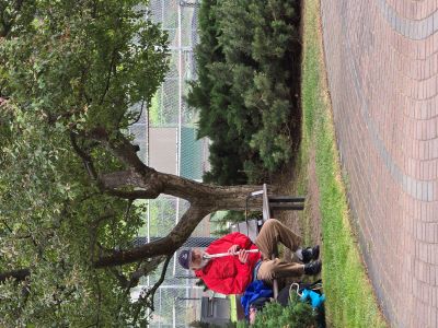 man in a red jacket on a park bench playing a flute