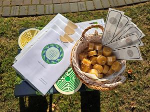 A table top with a collection of labyrinth booklets, a yellow labyrinth coaster, a red labyrinth coaster, a wicker basket of beeswax candles and black and white bookmarks. The background is green grass and brick pavers 