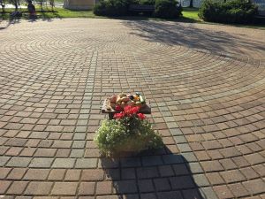 Photograph of an outdoor circular brick labyrinth, an altar with flowers and vegetables in the foreground 